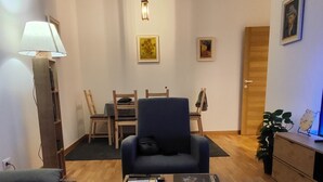 A living room with a sofa, a coffee table with paintings, a lamp, and a dining area with chairs and a table. - Cozy apartment in tranquil Podgorica with WiFi, AC (Podgorica)
