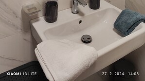 A bathroom with a white marble sink, a mirror, a towel, and a toothbrush holder. - Cozy apartment in tranquil Podgorica with WiFi, AC (Podgorica)