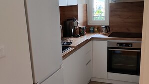 A compact kitchen with white cabinets, a stainless steel refrigerator, a built-in oven, and a window providing natural light. - Cozy apartment in tranquil Podgorica with WiFi, AC (Podgorica)