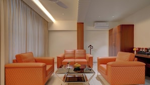 Una sala de estar moderna con una mesa de centro de vidrio, dos sofás naranjas y un sillón central.