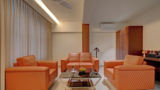 Una sala de estar moderna con una mesa de centro de vidrio, dos sofás naranjas y un sillón central.