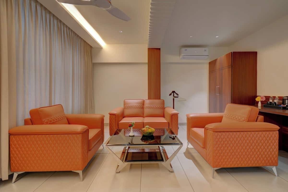A modern living room with a glass coffee table, two orange sofas, and a central armchair.