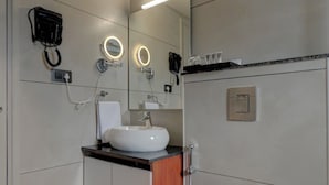 Un baño moderno con lavamanos blanco, un espejo con iluminación y secador de pelo, y un inodoro.