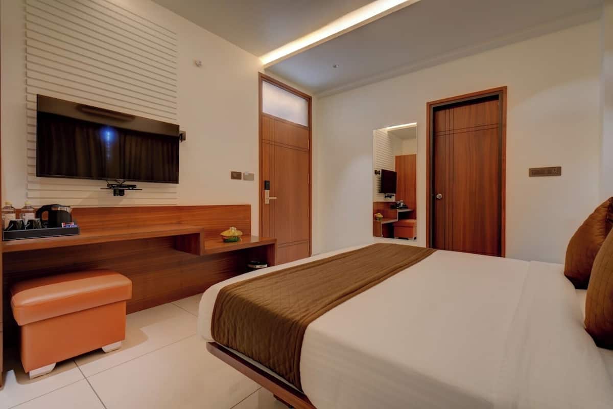 A hotel room with a bed, a desk with a chair, a TV, and a wardrobe.