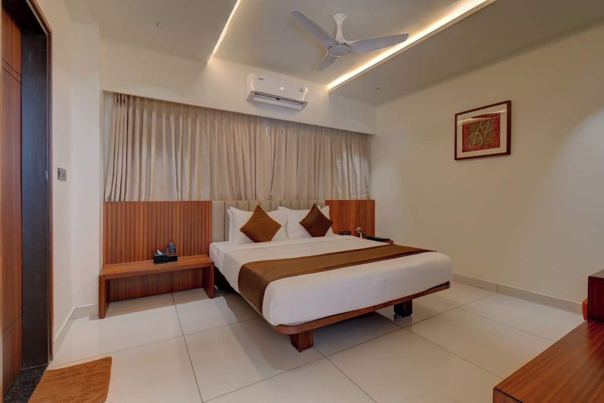 A modern hotel room with a large bed, wooden headboard, bedside tables, an air conditioning unit, a ceiling fan, and a framed artwork on the wall.
