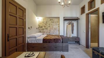 Un dormitorio con pared de piedra, cama, mesita de noche, perchero y maleta.