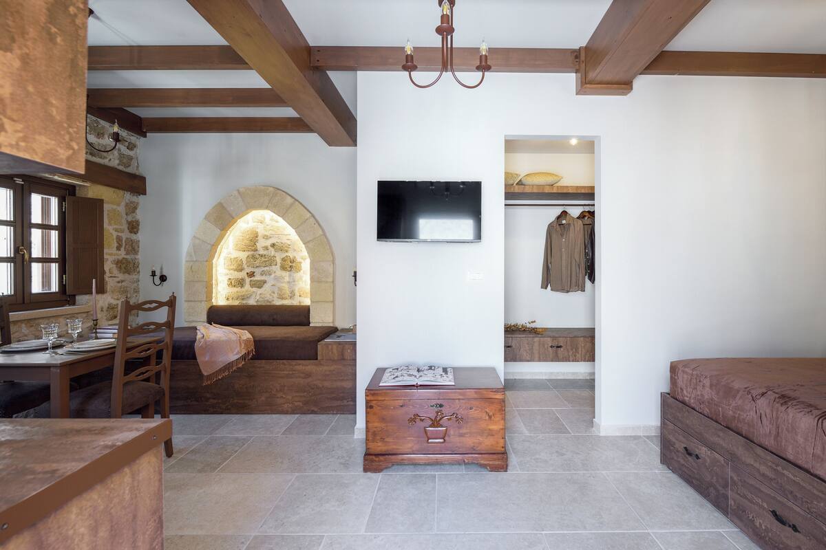 Una habitación acogedora con un arco de piedra, un cofre de madera, un televisor montado en la pared y una cama.