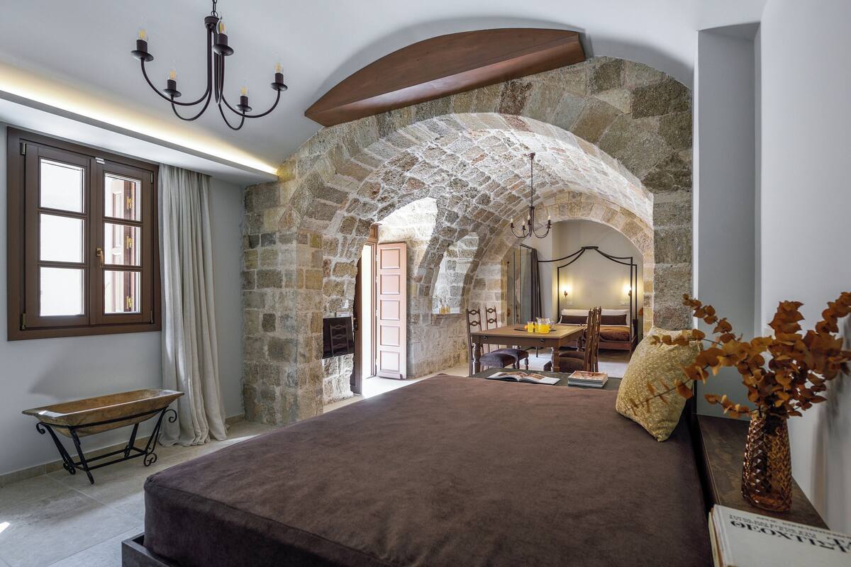 Un dormitorio con un arco de piedra, una cama, un banco y una zona de comedor.
