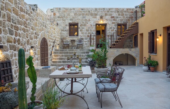 A stone courtyard with a table set for dining, surrounded by potted plants and a cactus.