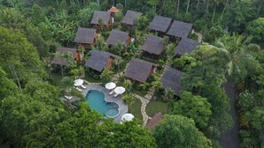 An aerial view of a resort with multiple thatched-roof cottages, a central swimming pool, and lush tropical vegetation. - Samujha Ubud Resort (Ubud)
