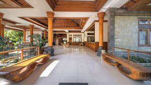 A spacious lobby with wooden benches, a glass railing, and a stone wall. - Samujha Ubud Resort (Ubud)