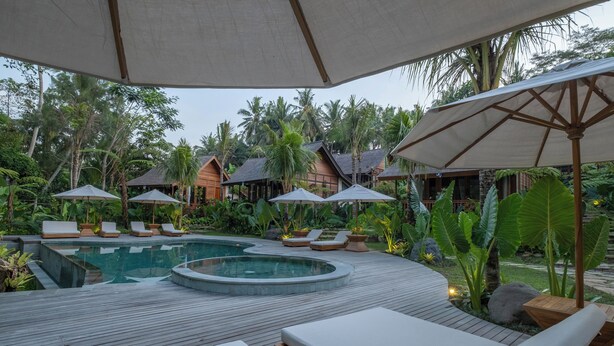 A pool area with lounge chairs and umbrellas, surrounded by tropical plants and wooden structures. - Samujha Ubud Resort (Ubud)