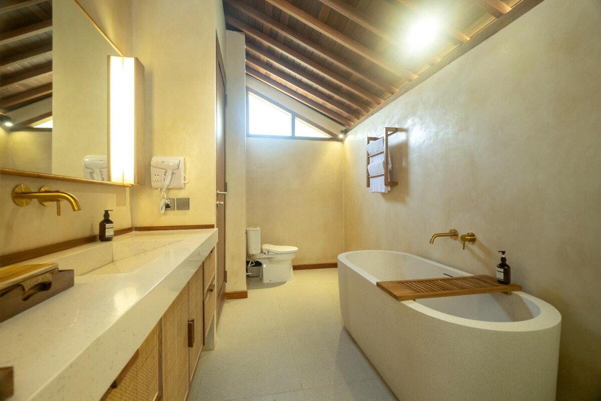 A modern bathroom with a large bathtub, a separate toilet, and a vanity with a mirror.