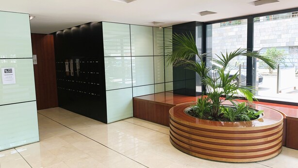 En moderne lobby med en glas elevator, en træbænk og en potteplante.