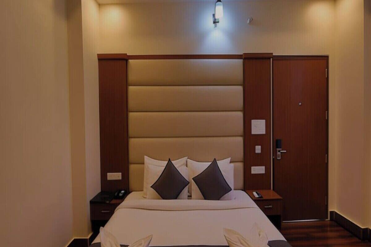A hotel room with a large bed, two bedside tables, a wooden wardrobe, and a ceiling light.