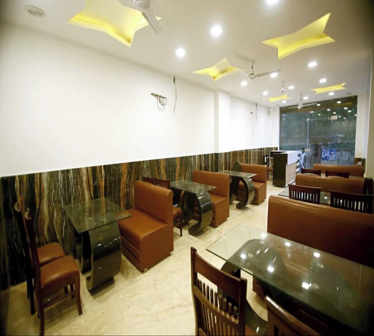 A restaurant with booths and tables, marble wall, ceiling lights, and a window.
