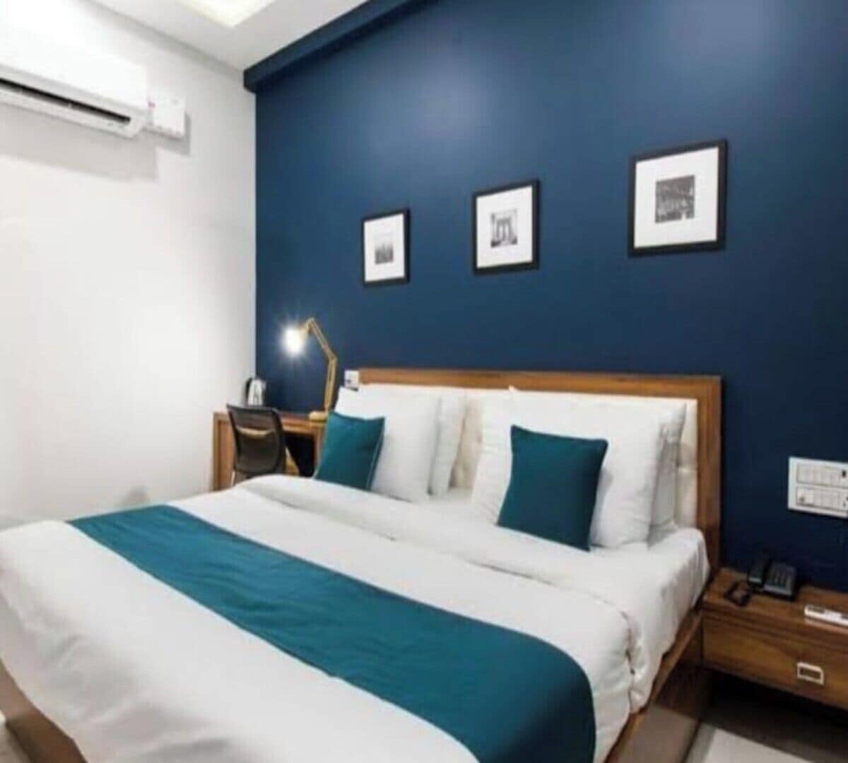 A hotel room with a large bed, a desk with a lamp, and three framed pictures on the wall.