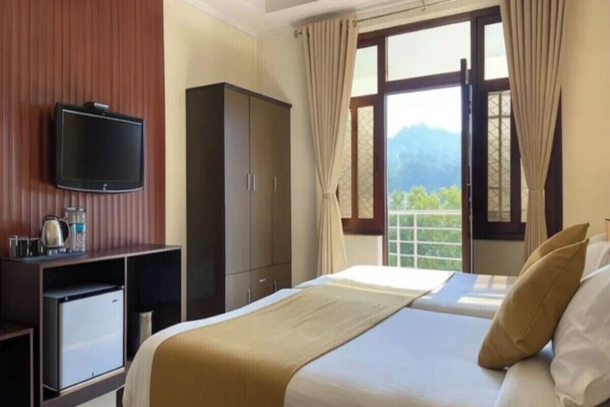 A hotel room with a bed, a TV, a wardrobe, and a window with curtains.