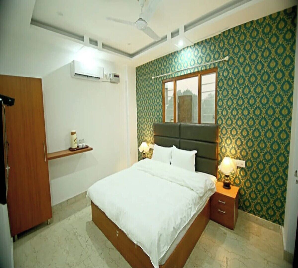 A bedroom with a bed, a nightstand with a lamp, a wardrobe, and patterned wallpaper.