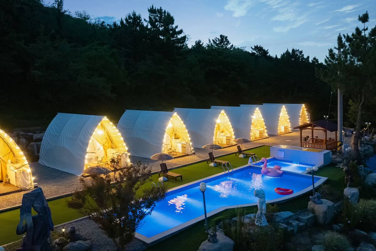 Une rangée de tentes en forme de dôme, éclairées de l’intérieur, une piscine avec un flotteur en forme de flamant rose et un kiosque.