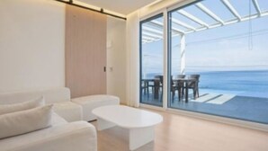 A modern living room with a white sofa, a white coffee table, and a glass door leading to a balcony with a view of the sea. - Space Yeongdeok (Yeongdeok)