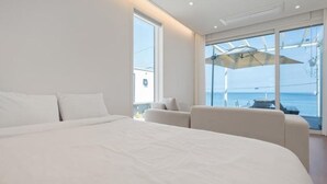 A modern bedroom with a large bed, a seating area, and a view of the sea through large windows. - Space Yeongdeok (Yeongdeok)