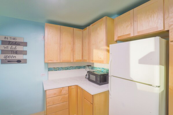 Una cocina con armarios de madera, un refrigerador blanco, un microondas y un cartel en la pared.