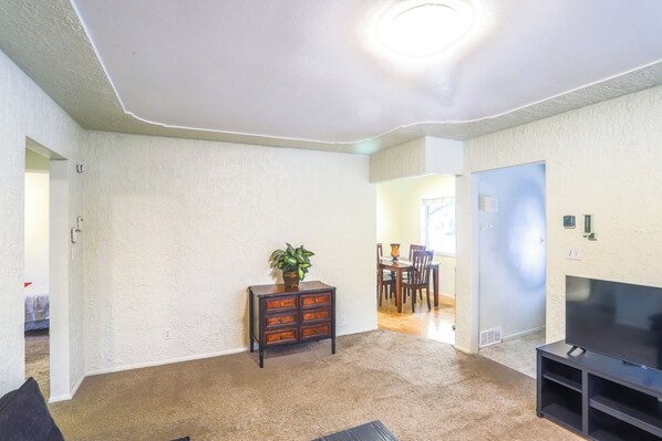 Una sala de estar con televisión, una planta y un mueble de madera.