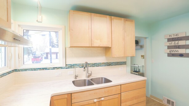 A kitchen with wooden cabinets, a double sink, and a window with a view of the outside.