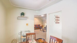 A dining area with a wooden table, chairs, and a decorative vase. There is a sofa and a coffee table in the background.