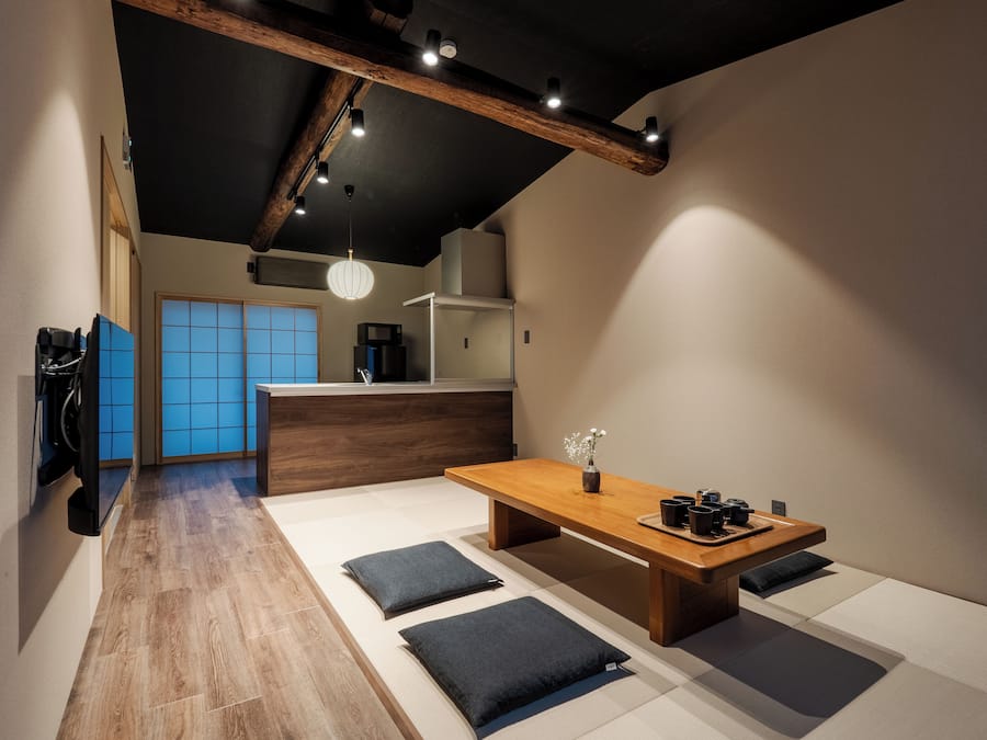 Un interior moderno con una mesa de comedor de madera, cojines negros y una puerta corredera tradicional japonesa al fondo.