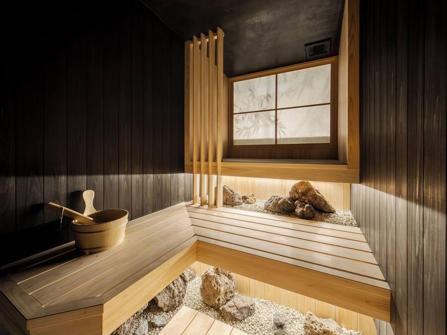 Perinteinen japanilainen onsen-kylpylä, jossa on puiset penkit, puinen ämpäri ja ikkuna, jonka lasi on himmennetty.