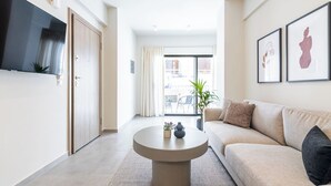 En moderne stue med en beige sofa, et rundt sofabord og et fladskærms-tv monteret på væggen.