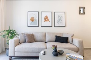 A living room with a sofa, a coffee table with a vase and bowl, and three framed artworks on the wall.