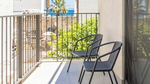 En balkon med to stole, gelænder af metal og udsigt over havet og palmer.