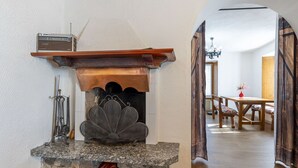 Une cheminée en pierre avec un paravent en métal, une étagère en bois et une radio posée sur le dessus.