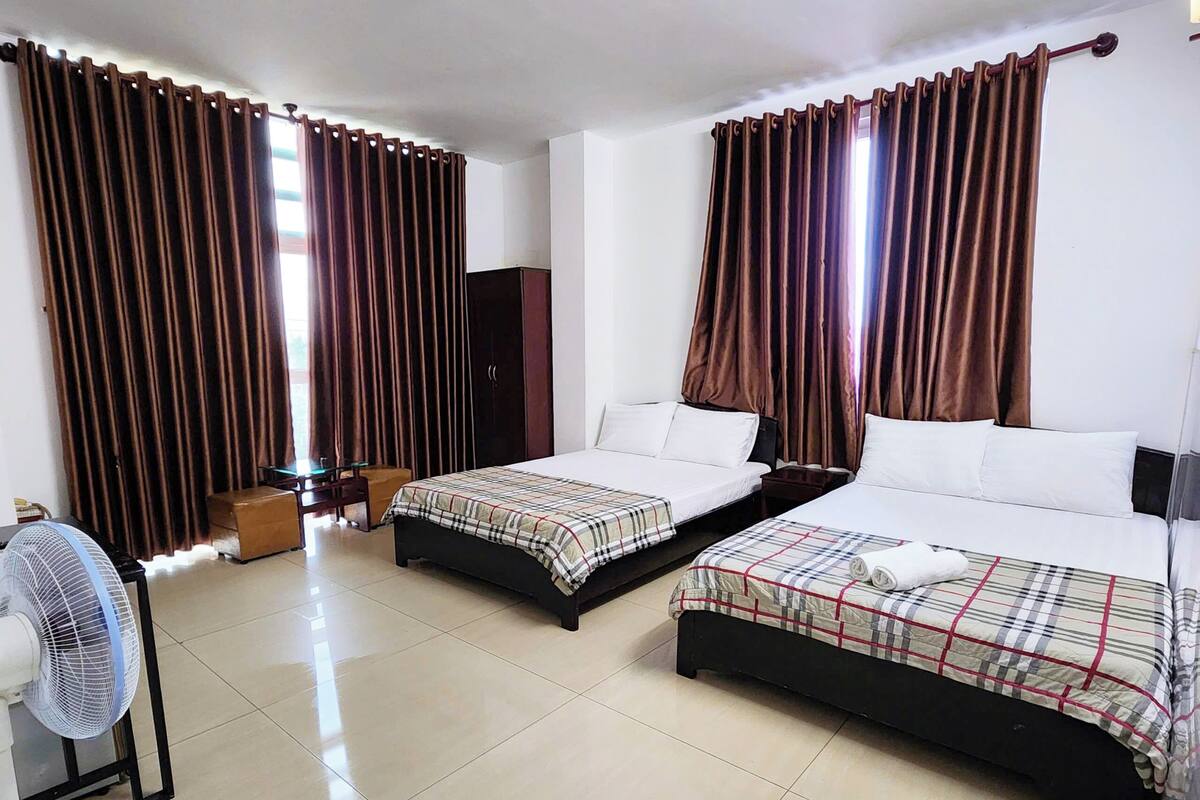 A hotel room with two beds, a desk, a chair, a fan, and a wardrobe.