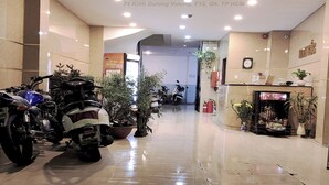 A hotel lobby with a reception desk, potted plants, and parked motorcycles. - Kinh Bac Hotel (Ho Chi Minh City)