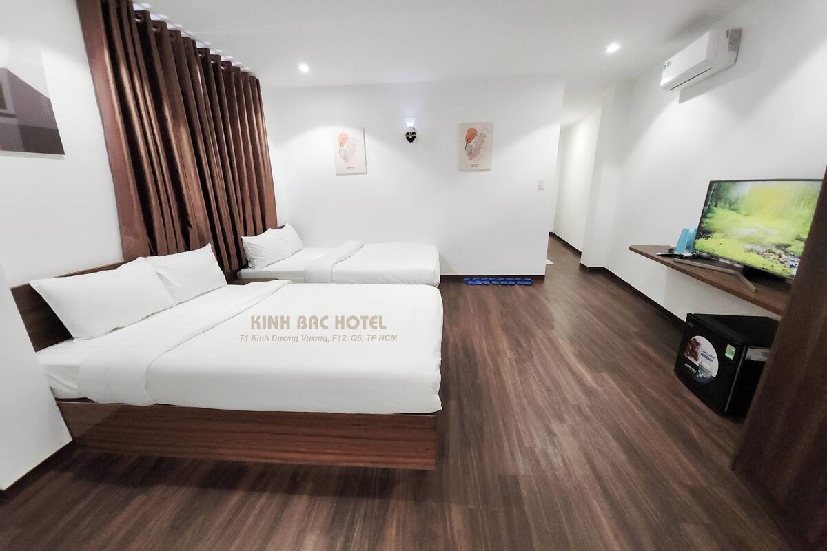 A hotel room with two beds, a TV, and a wooden floor.
