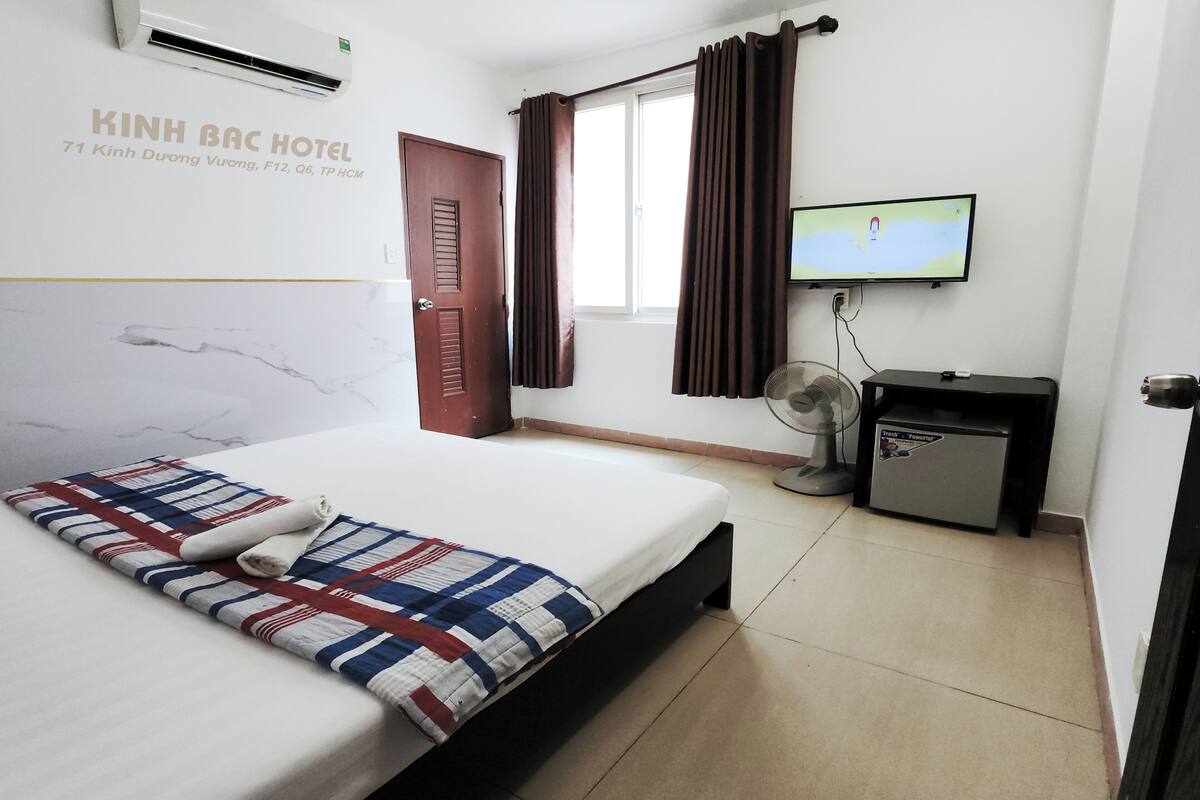 A hotel room with a bed, a TV, a desk with a fan, and a small refrigerator.
