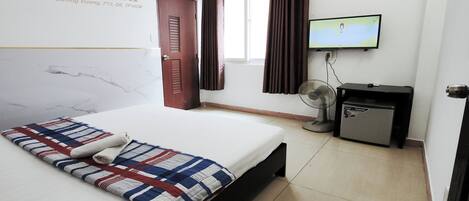 A hotel room with a bed, a TV, a desk with a fan, and a small refrigerator.