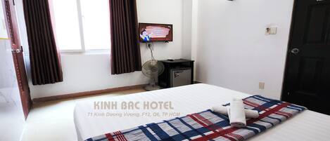Een hotelkamer met een bed, een televisie, een bureau en een raam met gordijnen.