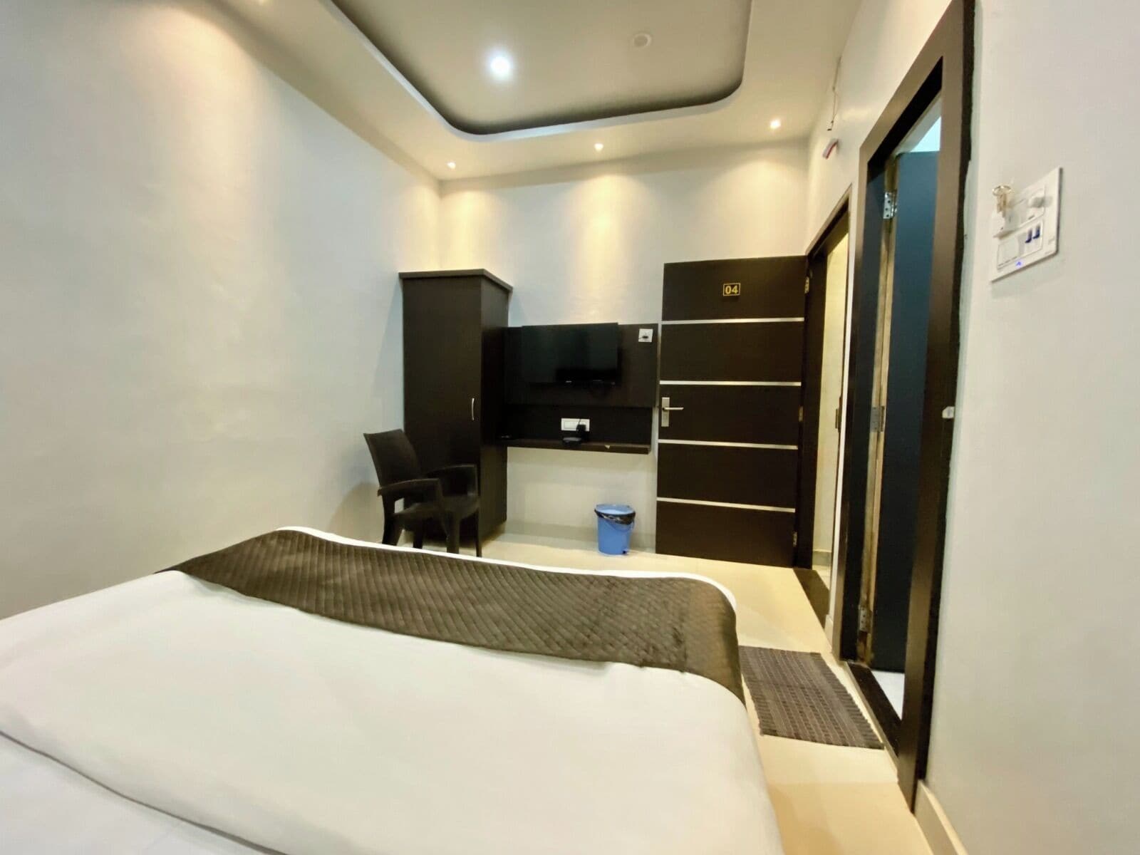 A modern hotel room with a bed, a desk, a TV, and a wardrobe.