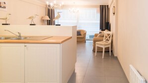 A modern kitchen with a central island, a dining area with a sofa and chairs, and a large window with curtains. - Duplex Apartment, 50m From Beach (Ostend)