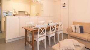 A modern kitchen with white cabinetry, a dining table set for four, and a beige sofa in the living area. - Duplex Apartment, 50m From Beach (Ostend)