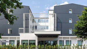 Een modern gebouw met een plat dak, grote ramen en een overdekt buitengebied met planten.