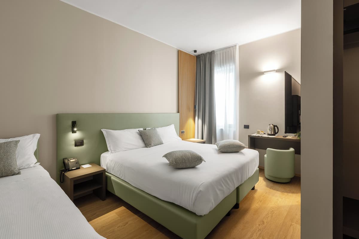 Ein Hotelzimmer mit zwei Betten, einem Schreibtisch mit Stuhl, einem Fernseher und einem Fenster mit Vorhängen.
