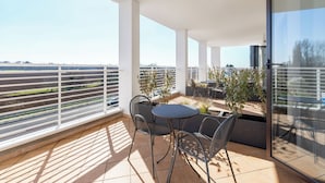 Een balkon met een tafel en stoelen, een glazen deur en uitzicht op een spoorlijn en groen.