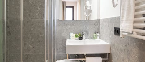 Un baño moderno con ducha envuelta en vidrio, un lavabo blanco y un banco.