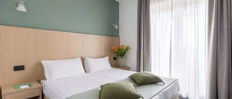 A hotel room with a bed, nightstand, lamp, and a window with curtains.